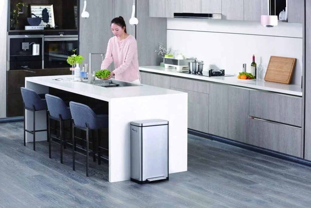 Thùng rác đạp chân EKO inox đặt cạnh đảo bếp trong căn bếp gia đình hiện đại, người dùng đang sơ chế rau tại đảo bếp
