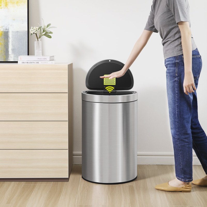 Người dùng mở nắp thùng rác inox tròn đặt cạnh tủ gỗ trong phòng khách